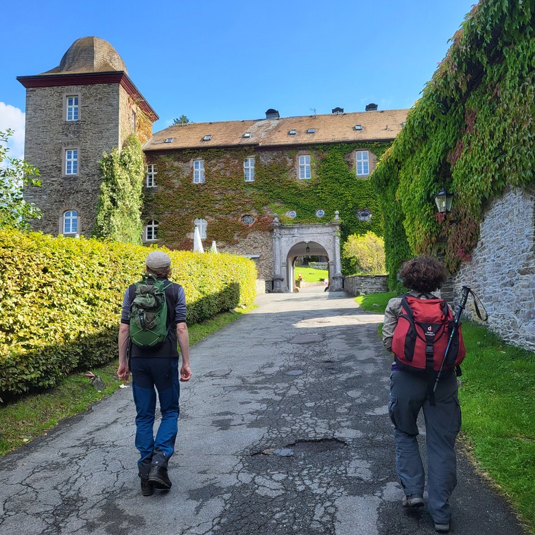 Zwei Personen laufen einen Weg entlang, der zur Burg Schnellenberg führt. Blauer Himmel.