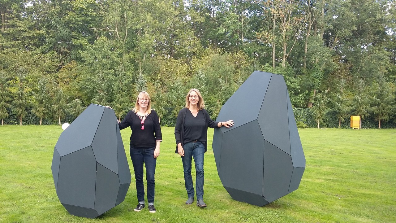 Zwei der Megalith-Modelle im direkten Größenvergleich mit Designerin Nora Franzmeier (links) und Geschäftsführerin der Altertumskommission Vera Brieske (rechts).