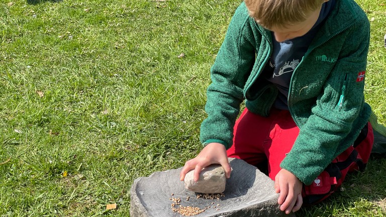 Ein Junge mahlt Korn mit Mahlstein und Läufer auf Steinzeit-Art (Foto: AKo/Lammers).